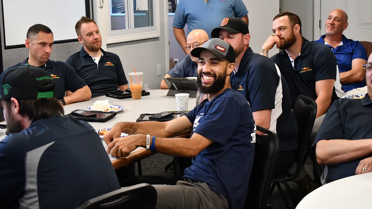 Action technicians in navy company shirts gathered around a table during a team meeting