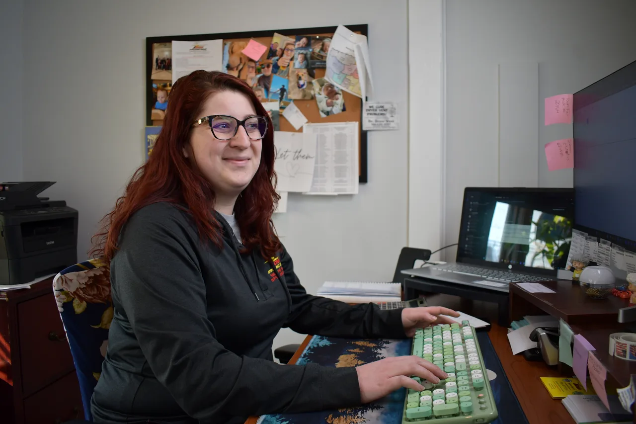 An Action office team member with red hair smiling while typing at her computer desk