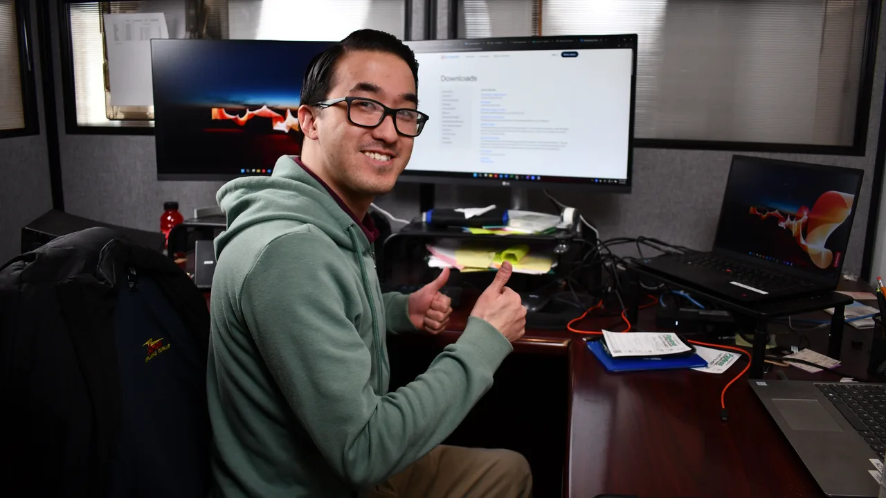 An Action office team member in a green hoodie smiling at his desk in front of two monitors