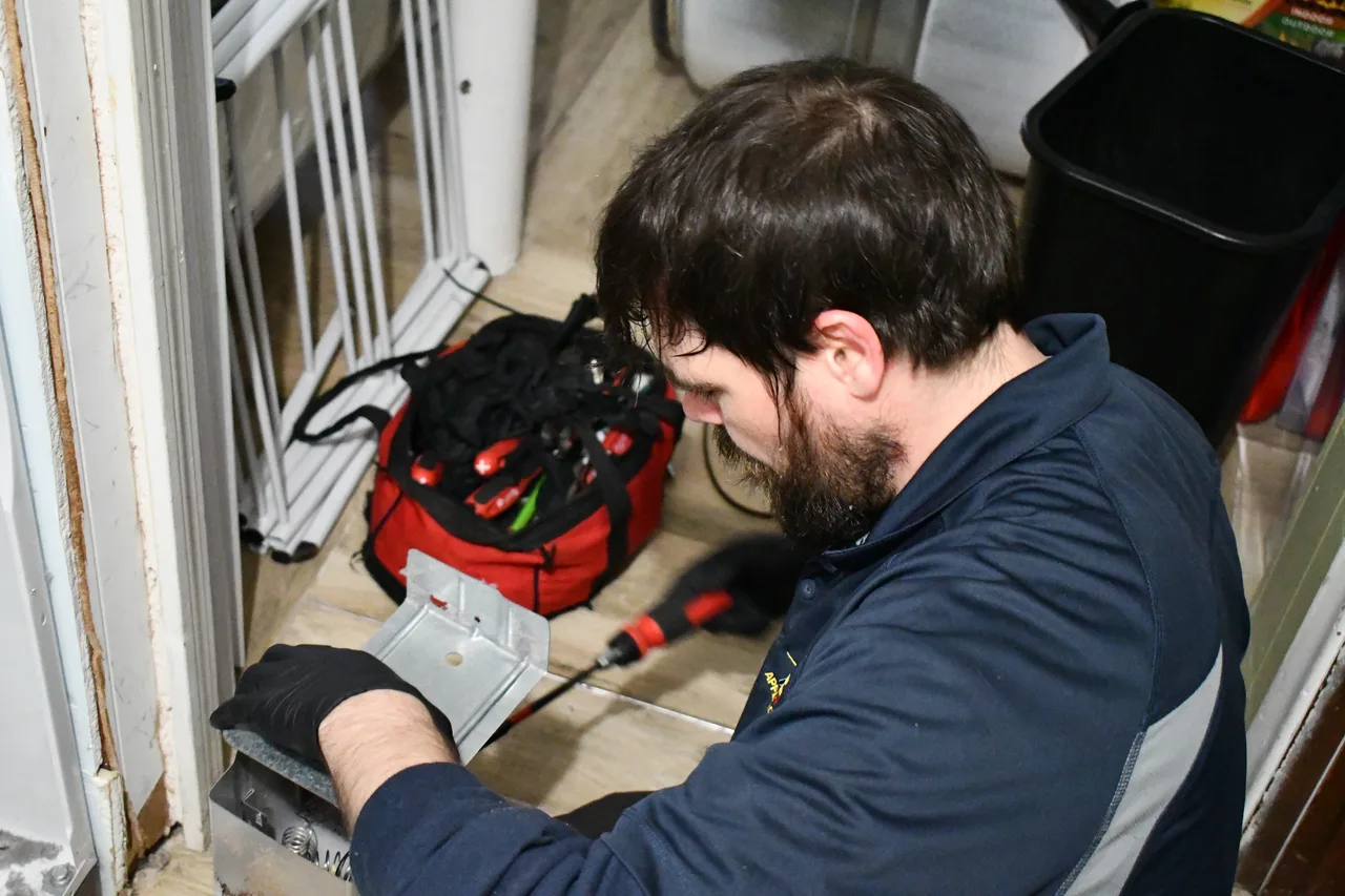 A technician in a navy jacket and work gloves using a red tool kit while repairing an appliance