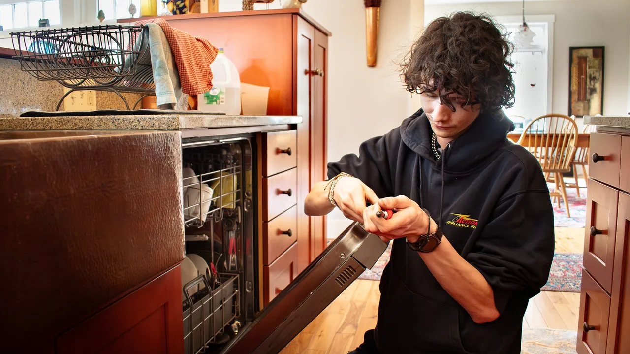 An Action technician working on the open door of a dishwasher in a home kitchen