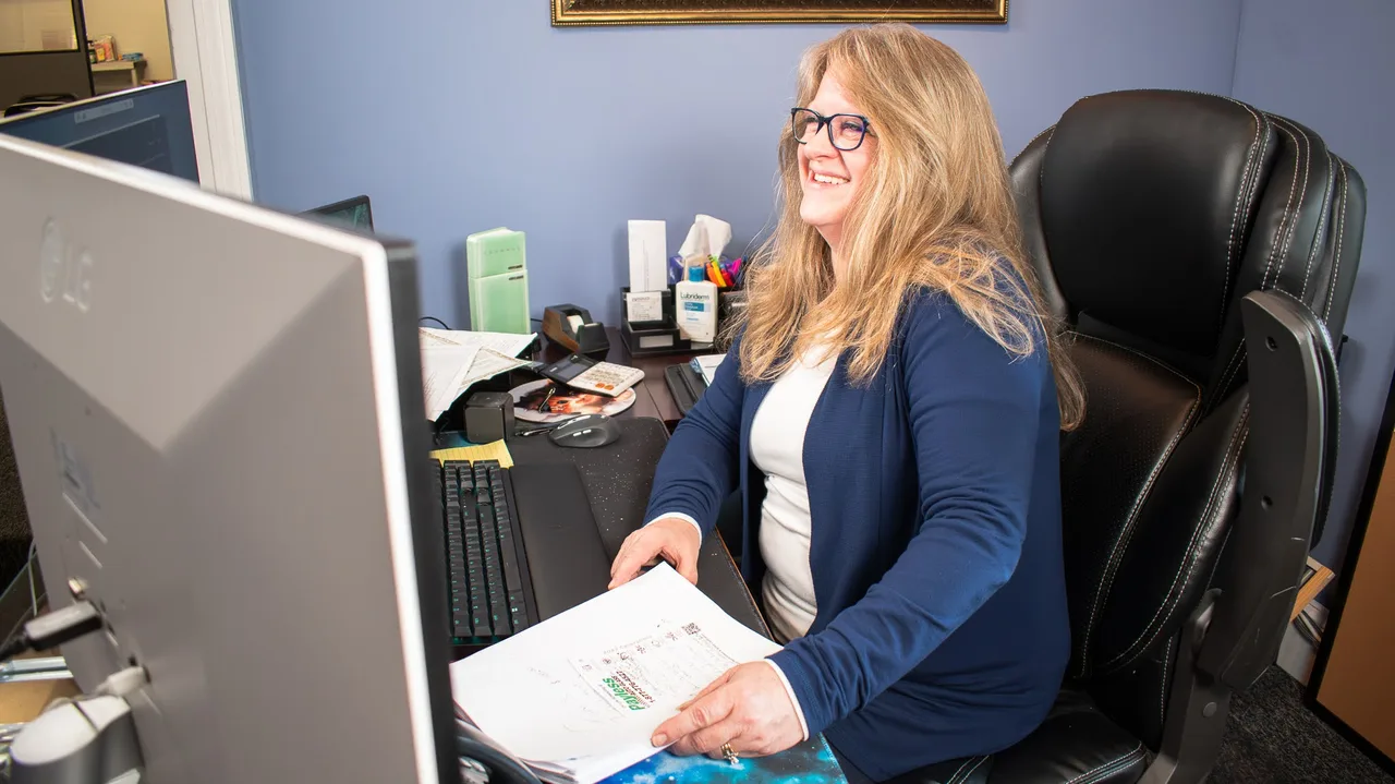 An Action office team member smiling at her desk beside her computer and paperwork