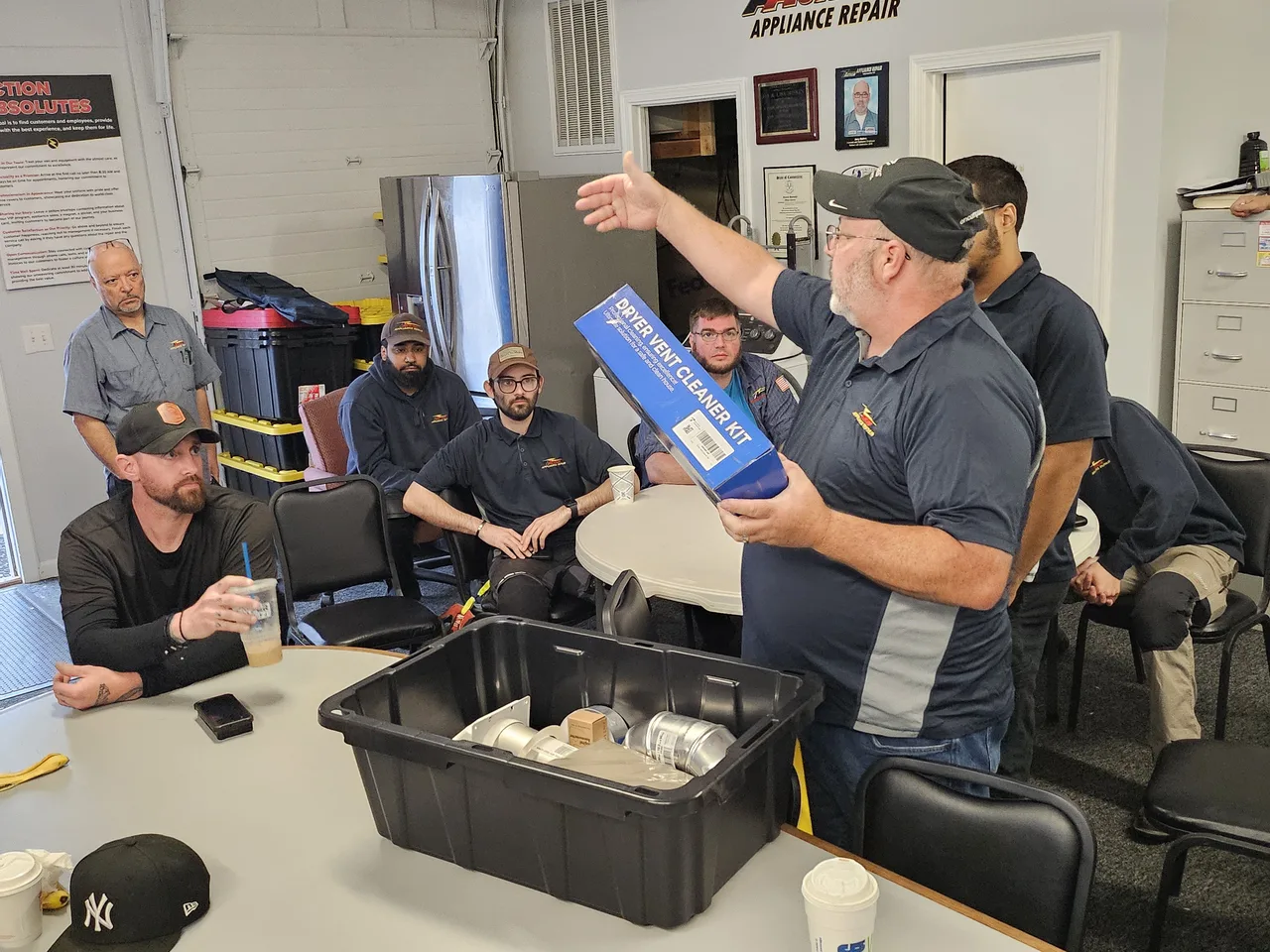 Action team members learning together as a colleague demonstrates a dryer vent cleaning kit at the office